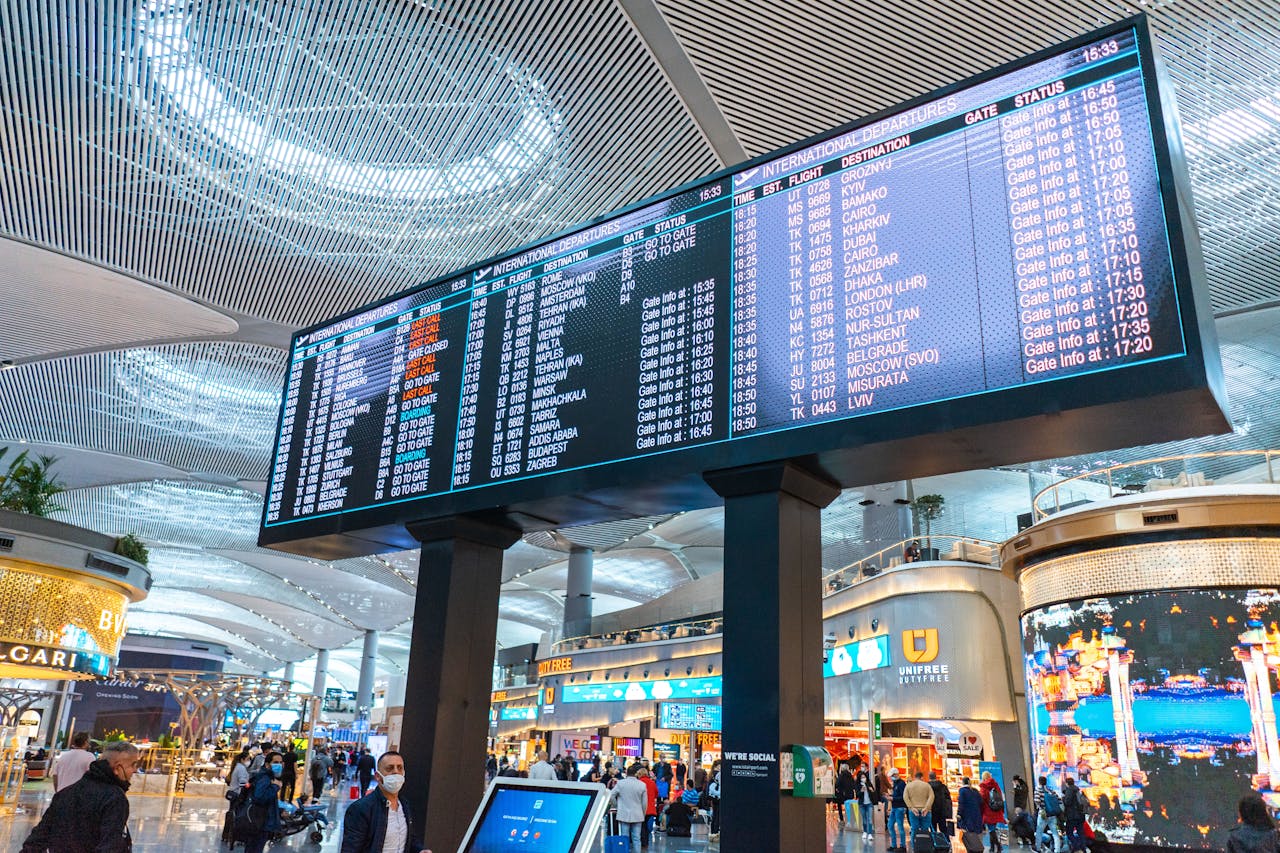 Passengers walk through Istanbul Airports departure area, surrounded by stores and flight information displays.